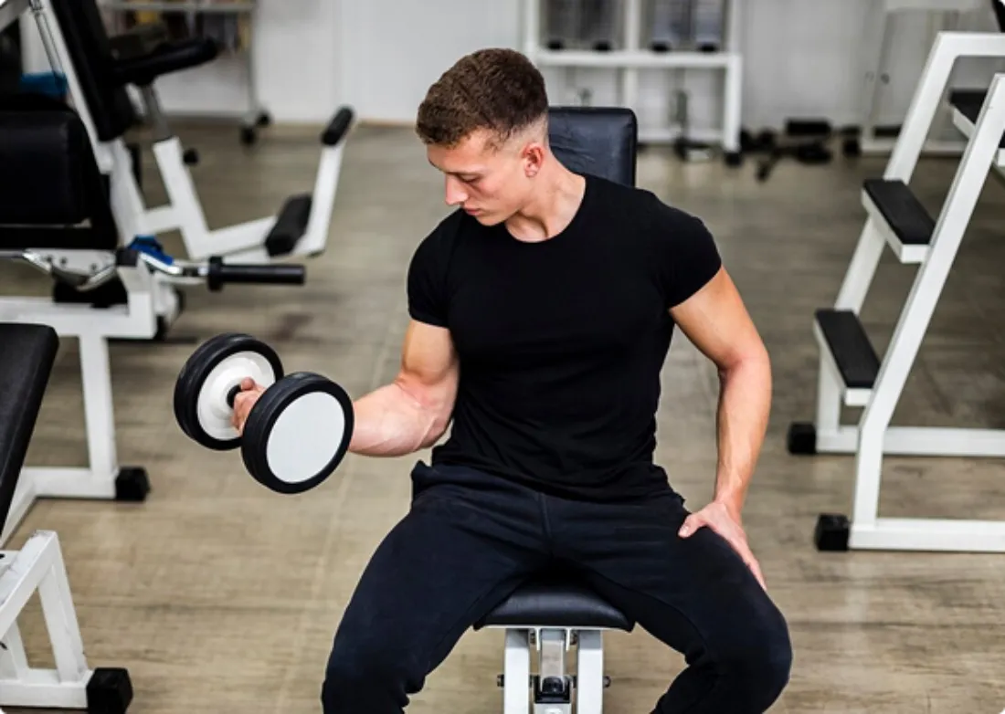 A man performs a dumbbell exercise in a gym, focusing on strength training with weights.