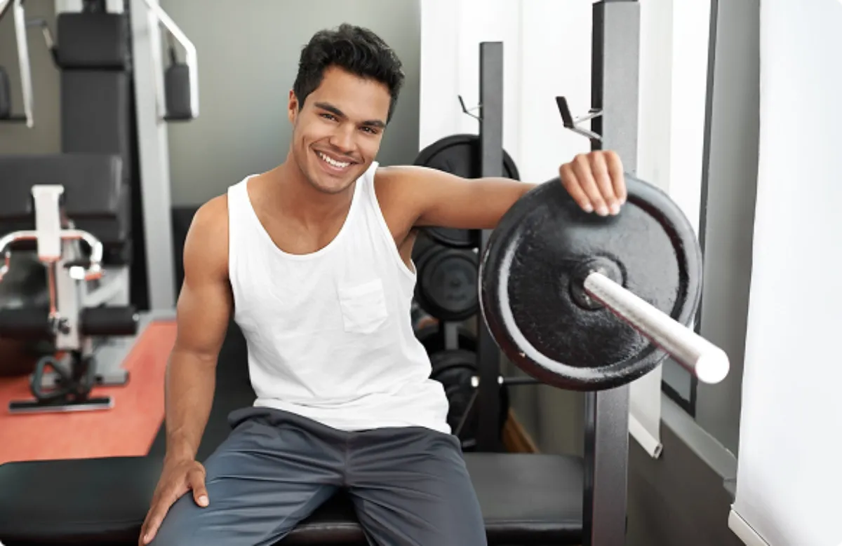 A smiling man holds a barbell, showcasing strength and enthusiasm in a fitness setting.