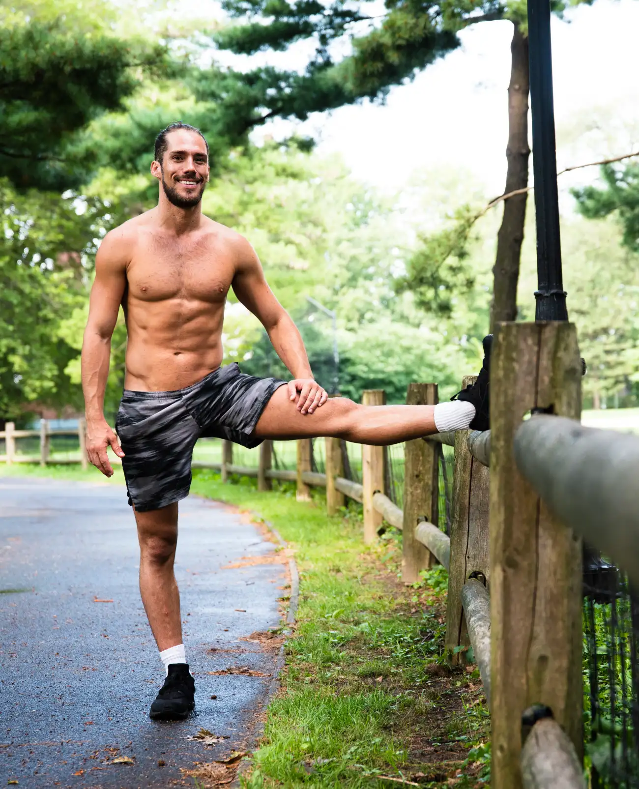 Man stretching outdoors by a fence in a park to improve flexibility and mobility.