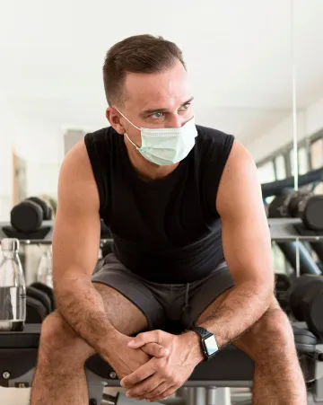 Front view of a man wearing a medical mask while working out in the gym for safety and protection
